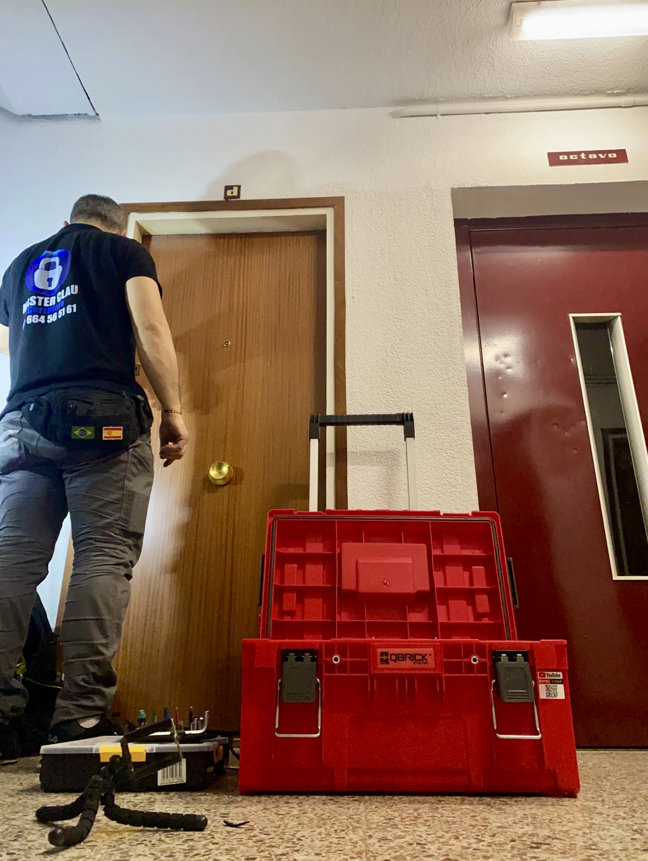Técnico inclinado junto a una puerta de madera, con caja roja de herramientas.